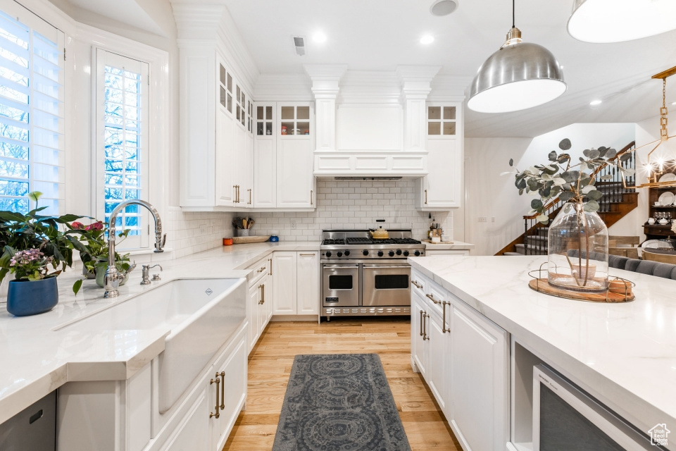 Kitchen featuring tasteful backsplash, light hardwood / wood-style flooring, double oven range, and decorative light fixtures