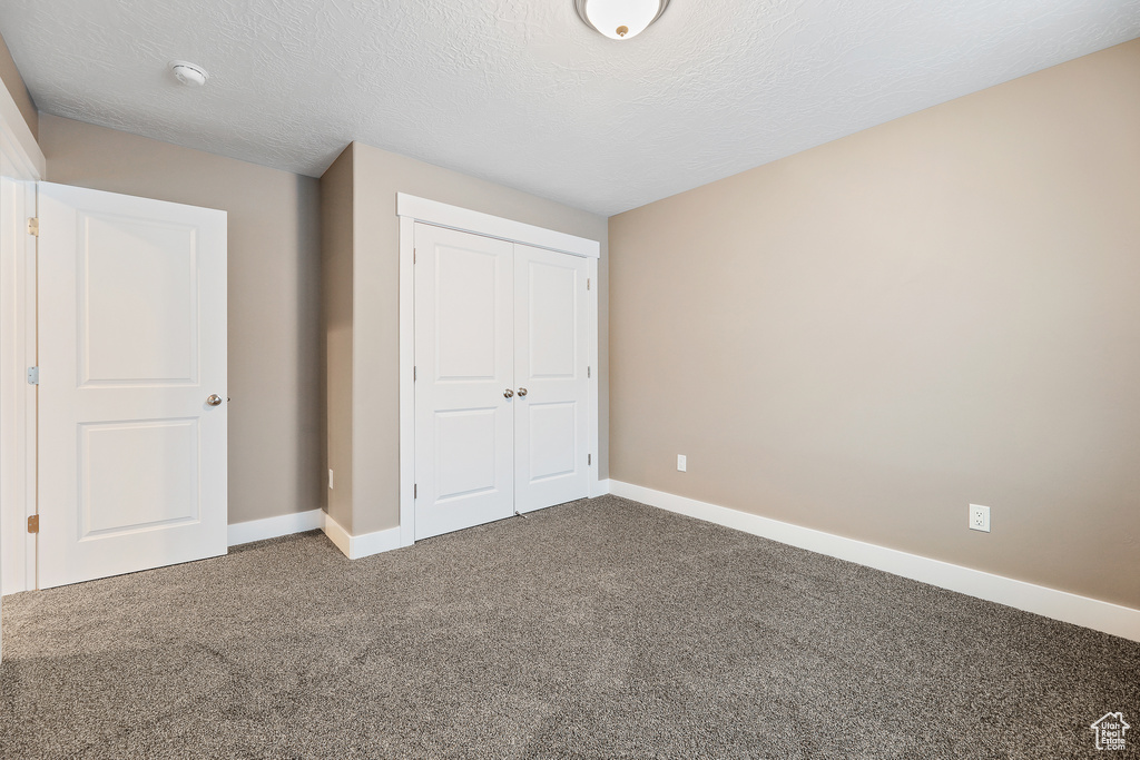 Unfurnished bedroom with dark colored carpet, a textured ceiling, and a closet