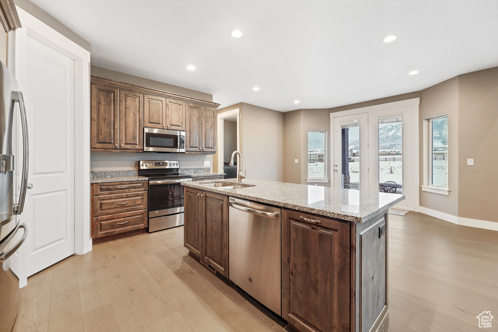 Kitchen with light wood-type flooring, stainless steel appliances, a kitchen island with sink, and sink