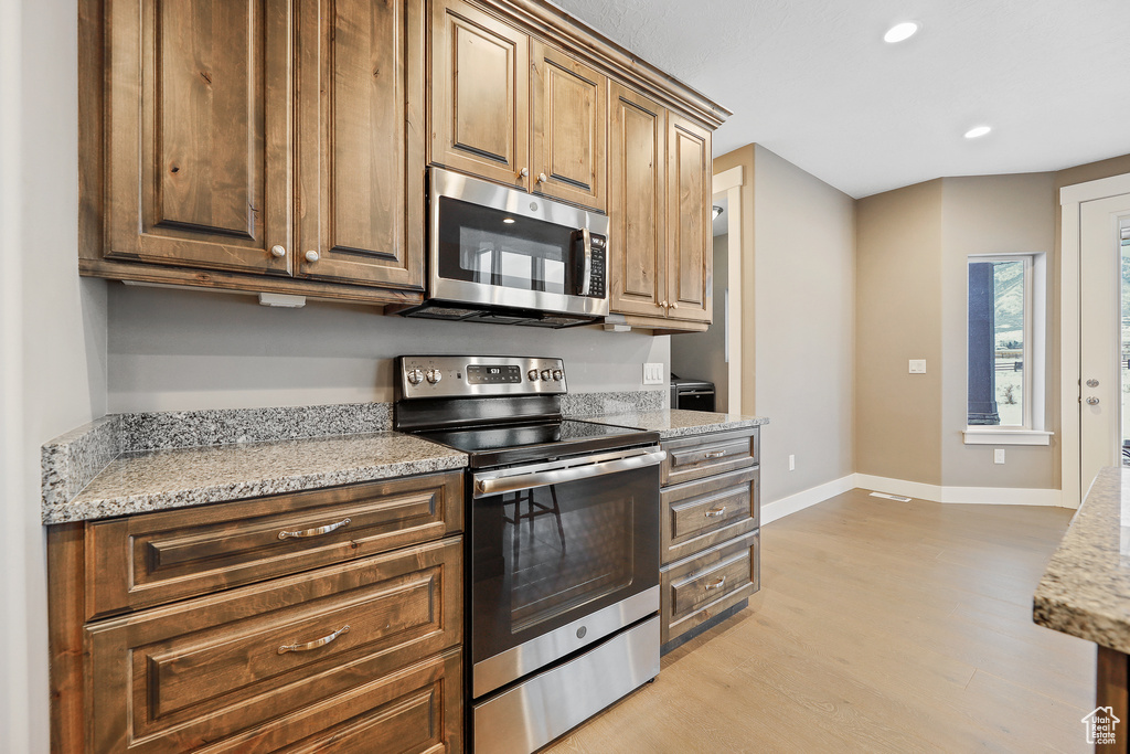 Kitchen with light hardwood / wood-style floors, appliances with stainless steel finishes, and light stone countertops