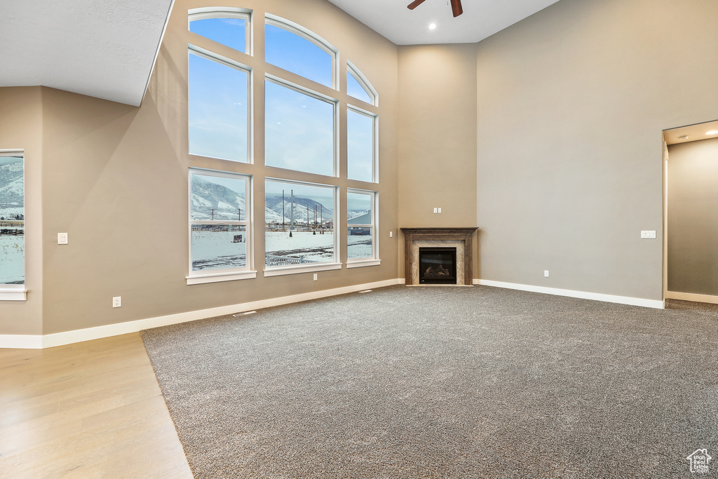 Unfurnished living room featuring light carpet, ceiling fan, and a high ceiling