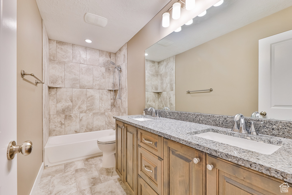 Full bathroom featuring tiled shower / bath, toilet, tile floors, vanity with extensive cabinet space, and dual sinks