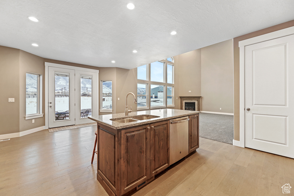Kitchen featuring light hardwood / wood-style floors, sink, dishwasher, and a kitchen island with sink
