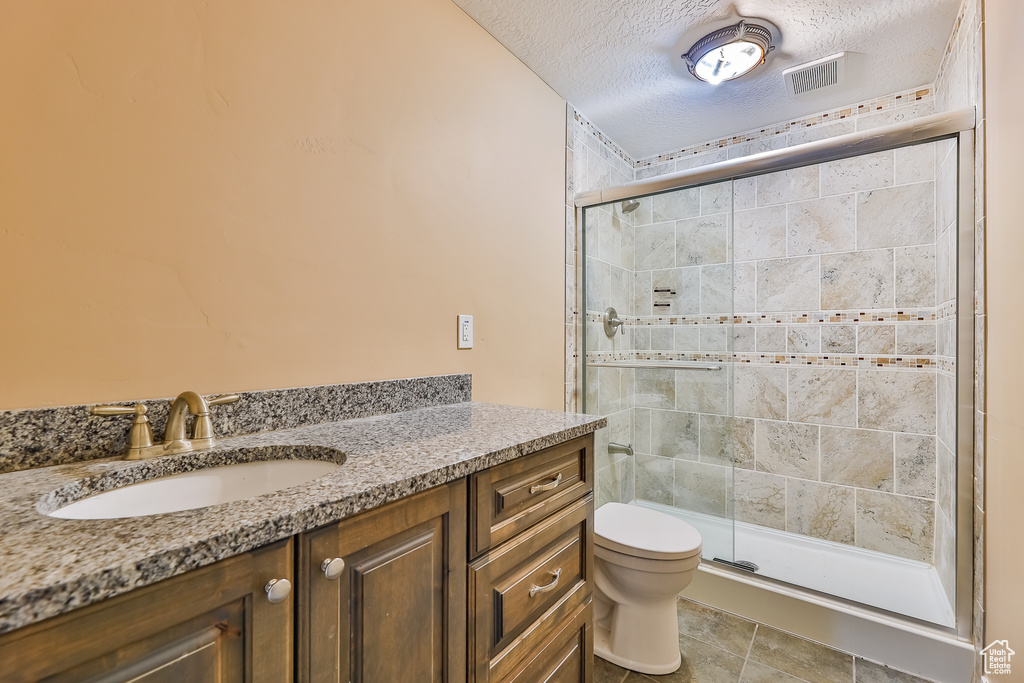 Bathroom with vanity, a textured ceiling, toilet, a shower with shower door, and tile floors