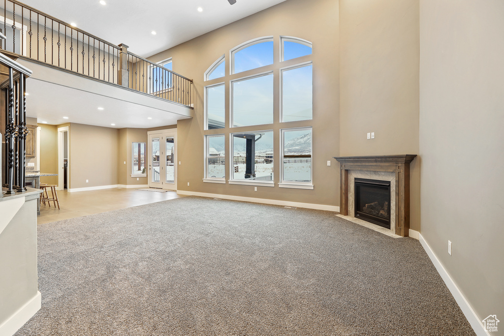 Unfurnished living room featuring a towering ceiling, light colored carpet, and french doors
