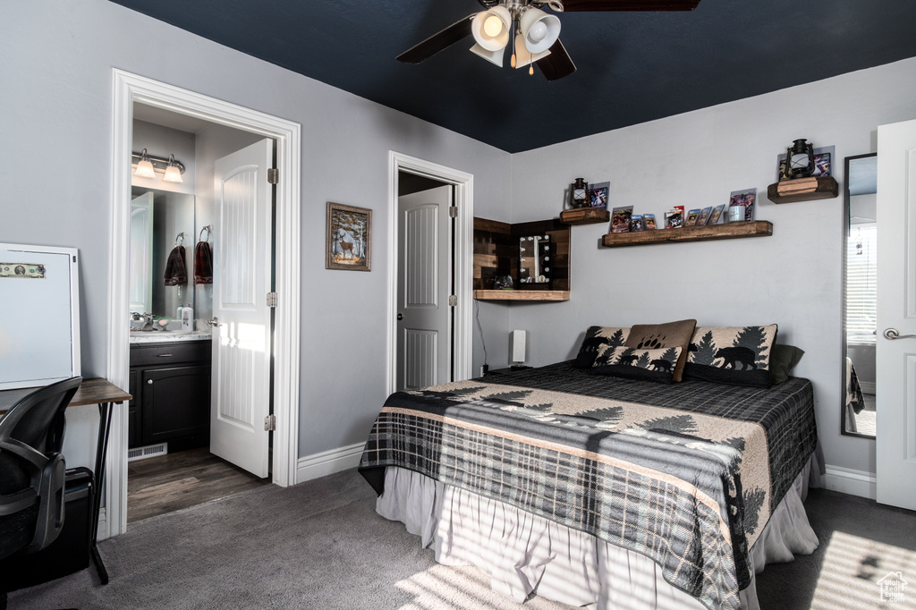 Bedroom with connected bathroom, dark colored carpet, and ceiling fan