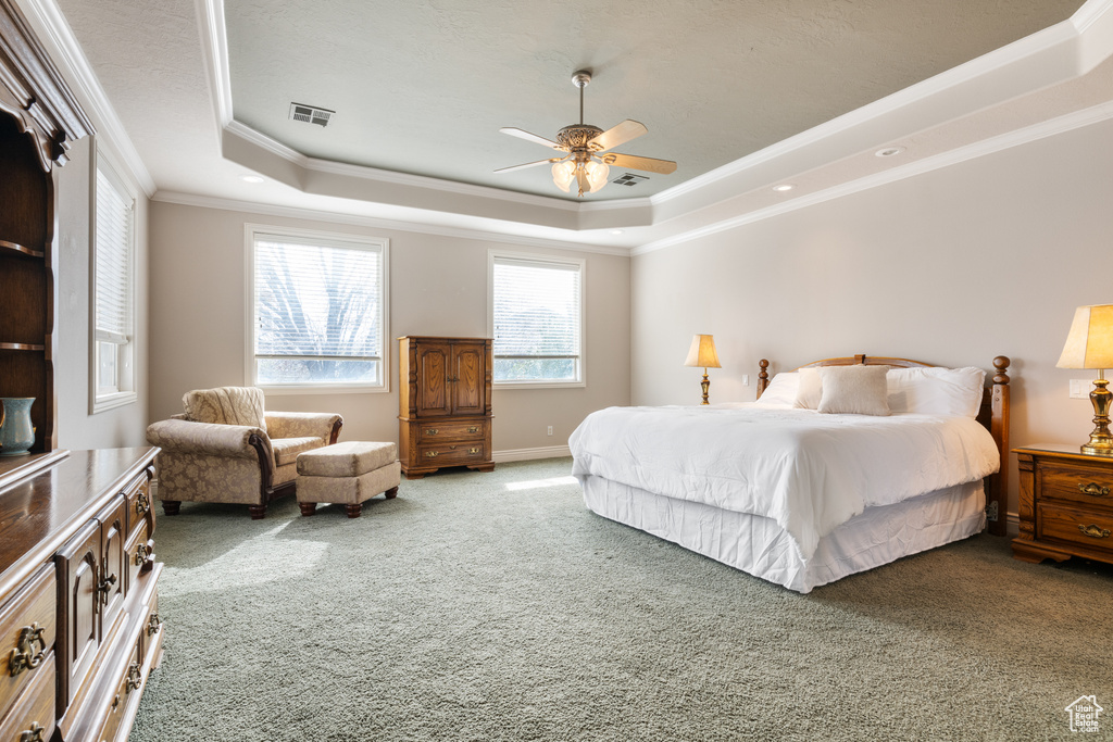 Carpeted bedroom featuring ornamental molding, ceiling fan, and a raised ceiling