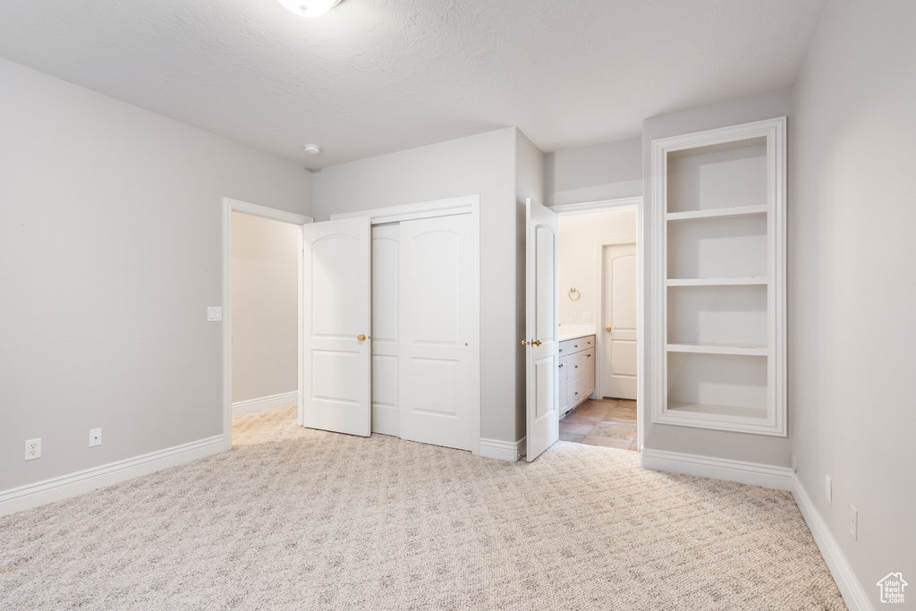 Unfurnished bedroom featuring connected bathroom, a closet, and light colored carpet