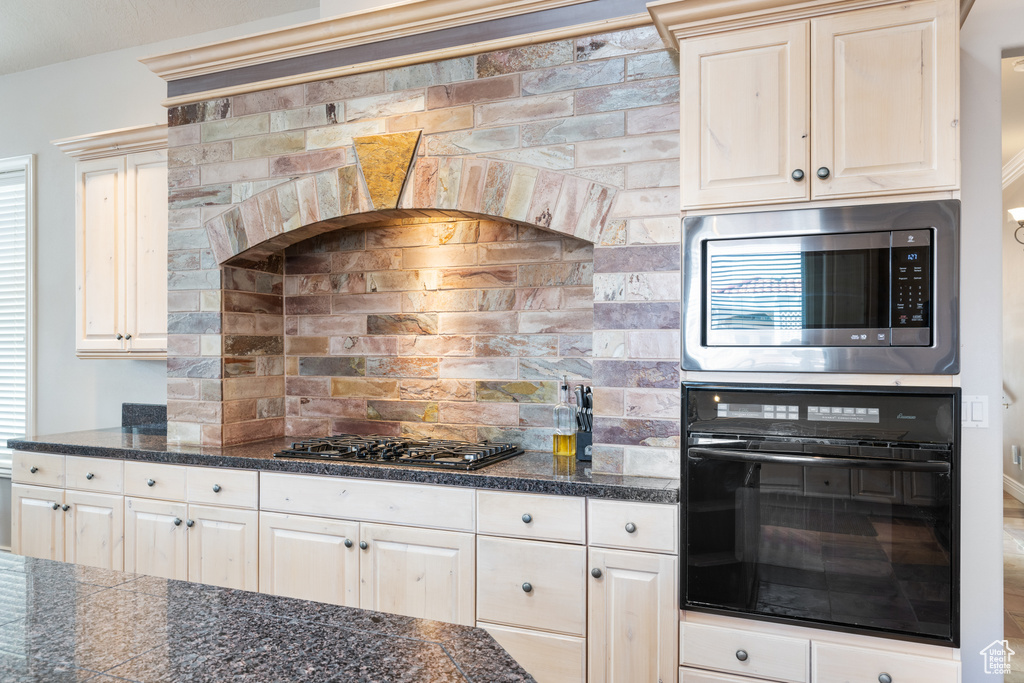 Kitchen with brick wall, black appliances, backsplash, and white cabinets