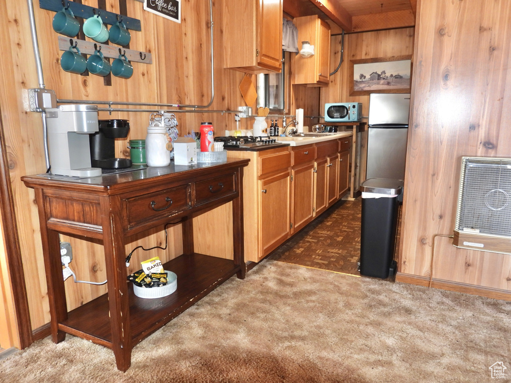 Kitchen with wood walls, dark carpet, sink, and stainless steel fridge