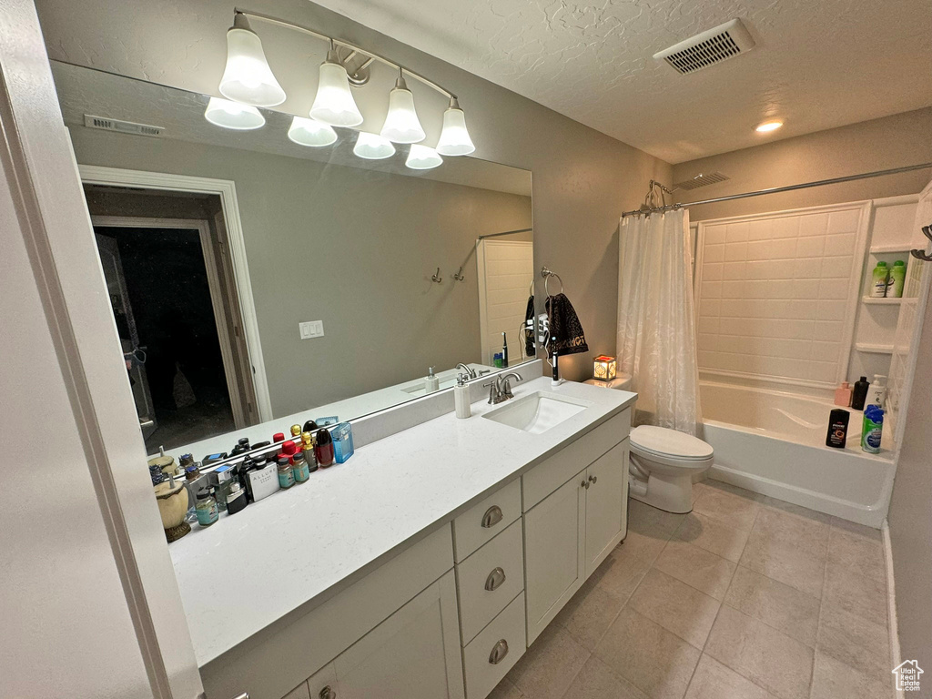 Full bathroom featuring shower / bath combo with shower curtain, a textured ceiling, vanity with extensive cabinet space, toilet, and tile floors