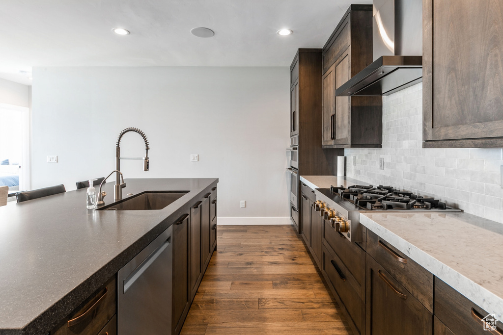 Kitchen with tasteful backsplash, dark hardwood / wood-style flooring, sink, appliances with stainless steel finishes, and wall chimney range hood