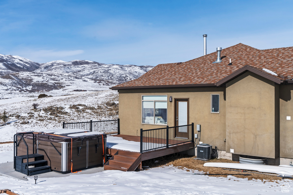 Snow covered rear of property with central AC, a hot tub, and a wooden deck