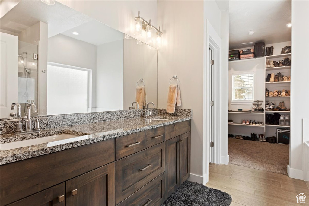 Bathroom with a shower with shower door, double sink, vanity with extensive cabinet space, and tile flooring