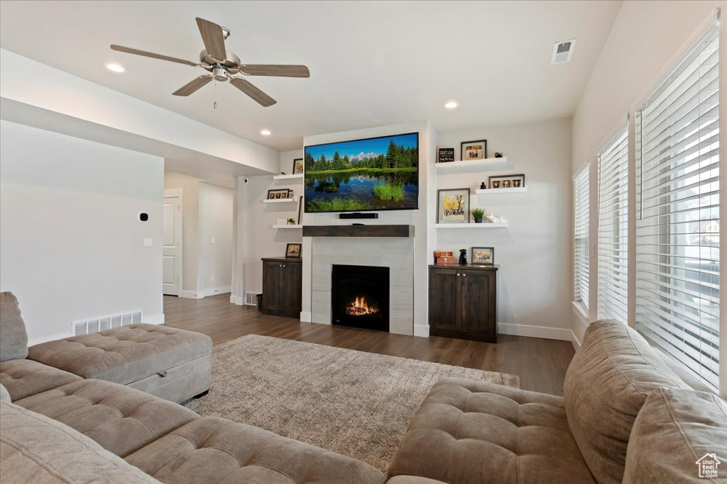 Living room with dark wood-type flooring, a tile fireplace, and ceiling fan