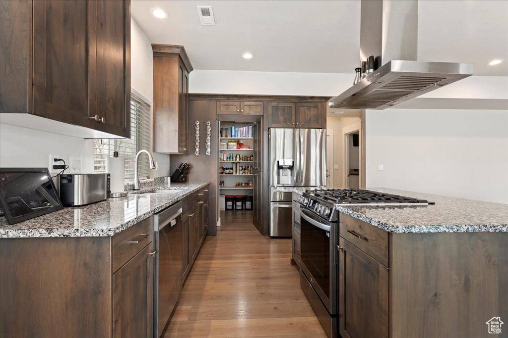 Kitchen with light hardwood / wood-style flooring, light stone countertops, island exhaust hood, sink, and appliances with stainless steel finishes