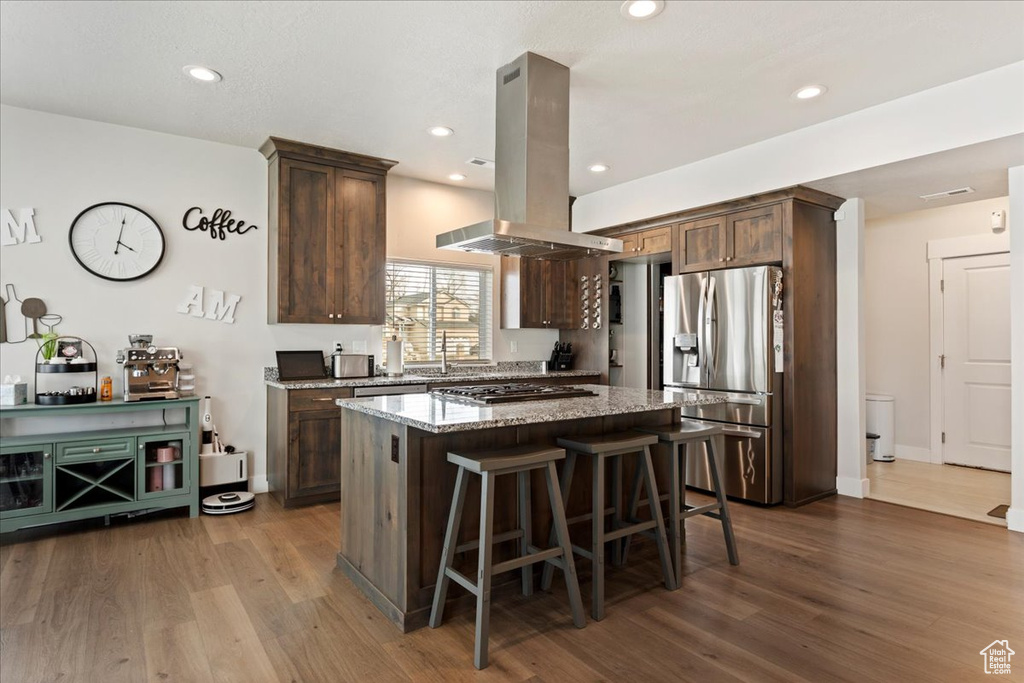 Kitchen with island range hood, a kitchen island, dark wood-type flooring, light stone countertops, and appliances with stainless steel finishes