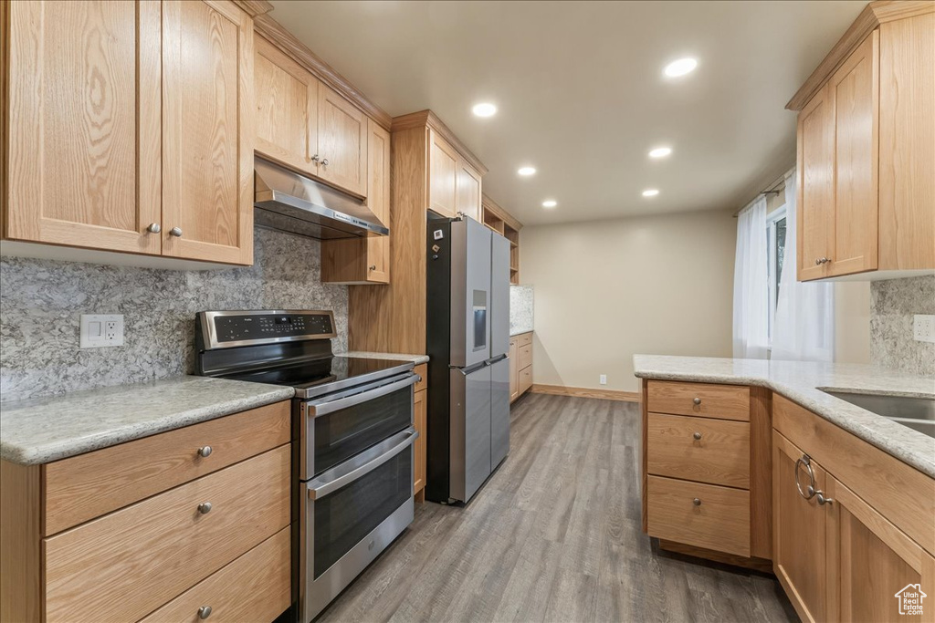 Kitchen with hardwood / wood-style floors, appliances with stainless steel finishes, light brown cabinets, and tasteful backsplash