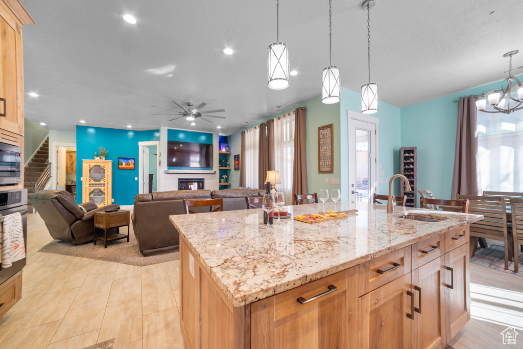 Kitchen with ceiling fan with notable chandelier, light stone countertops, a kitchen island with sink, sink, and decorative light fixtures