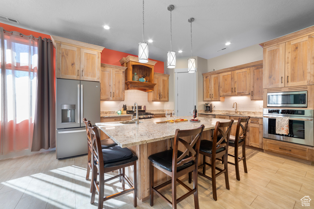 Kitchen with a wealth of natural light, appliances with stainless steel finishes, pendant lighting, and a kitchen bar