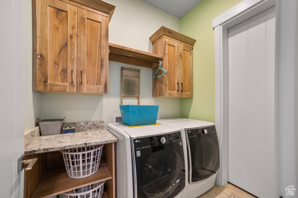 Washroom with hookup for a washing machine, light hardwood / wood-style flooring, washing machine and dryer, and cabinets