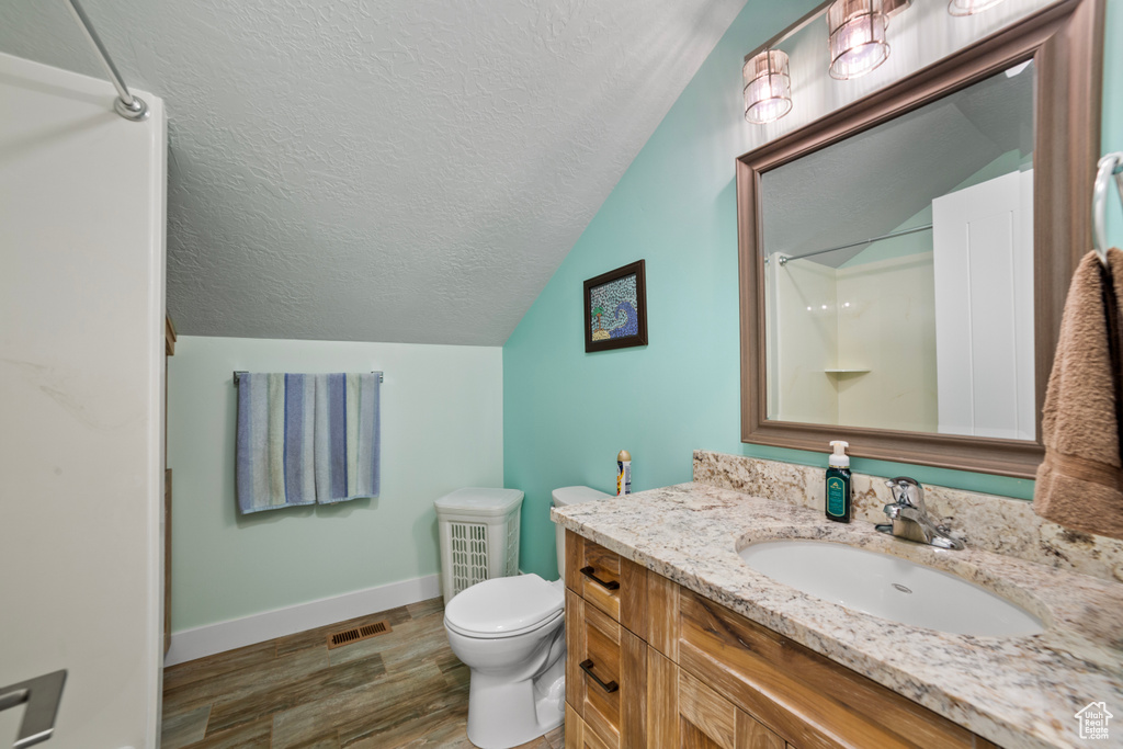 Bathroom with hardwood / wood-style floors, vanity, a textured ceiling, toilet, and vaulted ceiling