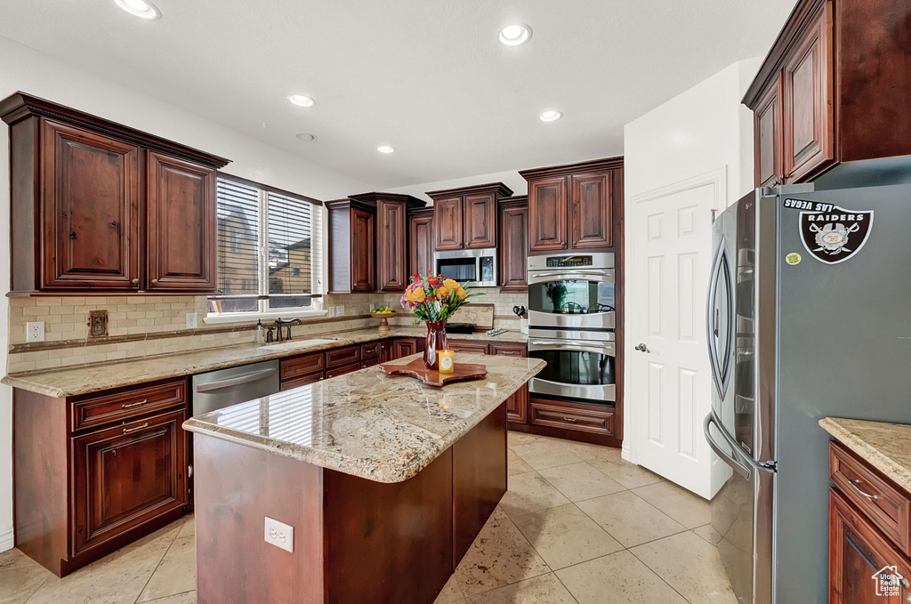 Kitchen with tasteful backsplash, light tile flooring, appliances with stainless steel finishes, and a kitchen island