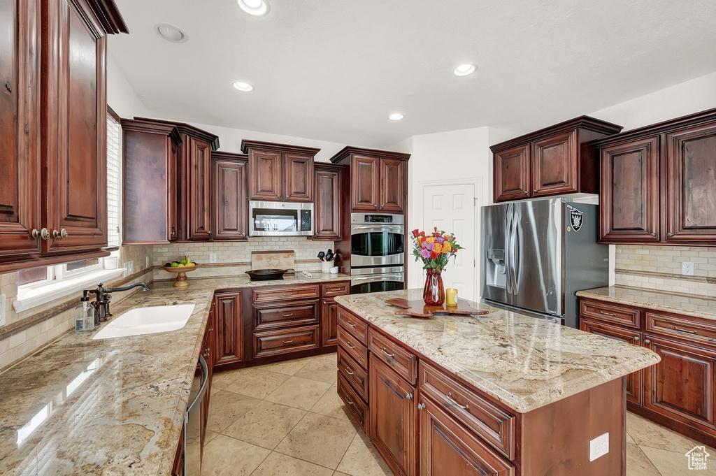 Kitchen featuring a center island, tasteful backsplash, sink, light tile floors, and appliances with stainless steel finishes