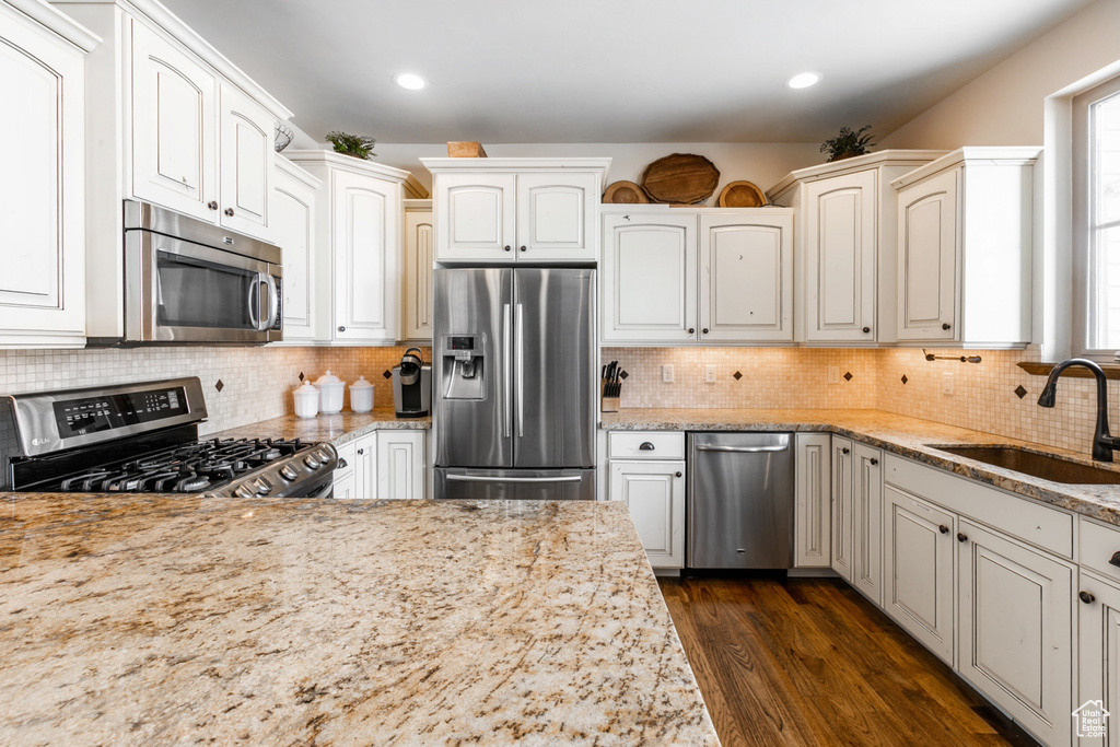 Kitchen featuring dark hardwood / wood-style flooring, stainless steel appliances, white cabinetry, tasteful backsplash, and sink