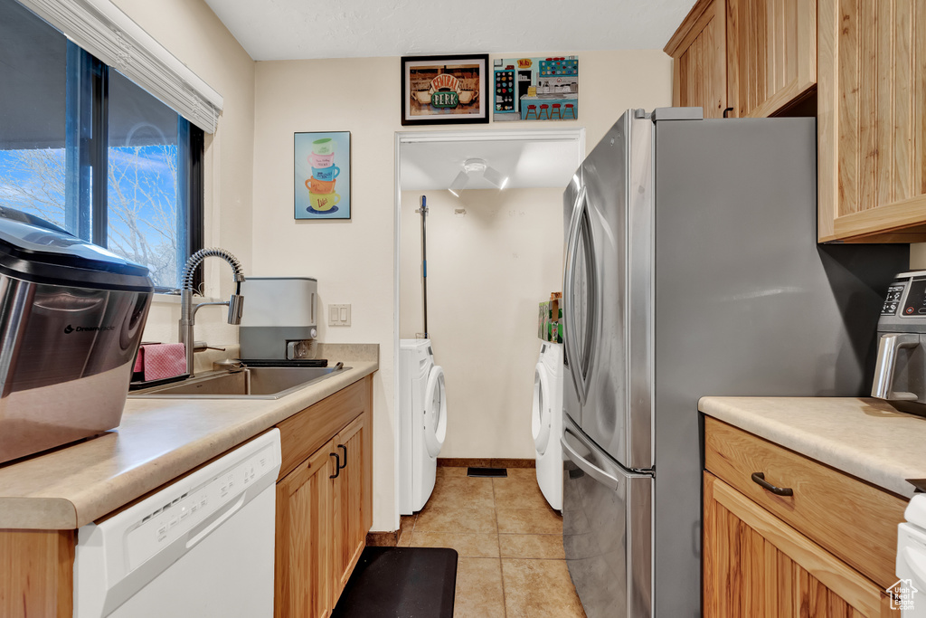Kitchen with white dishwasher, stainless steel refrigerator, sink, light tile floors, and washer and dryer