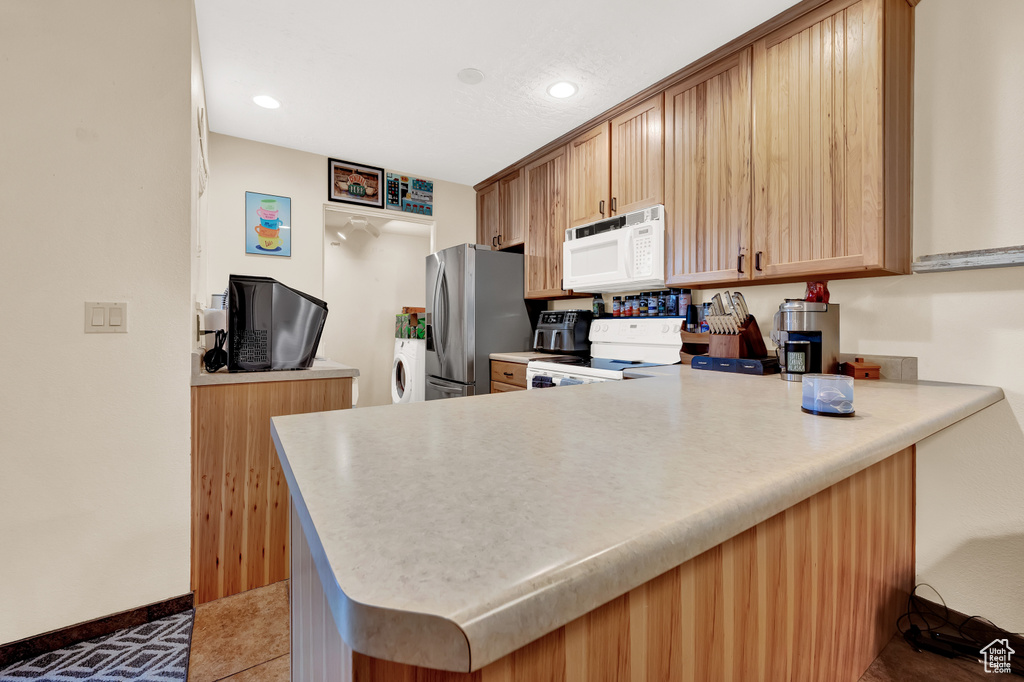 Kitchen featuring white appliances, tile flooring, washer and dryer, and kitchen peninsula