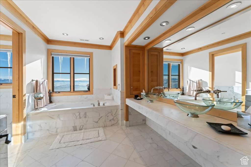 Bathroom featuring vanity, tiled tub, crown molding, and tile flooring