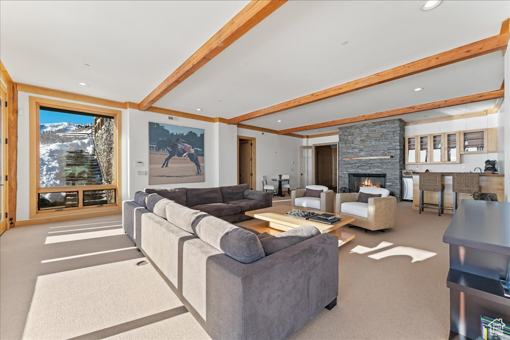 Living room featuring a stone fireplace, beamed ceiling, and light carpet