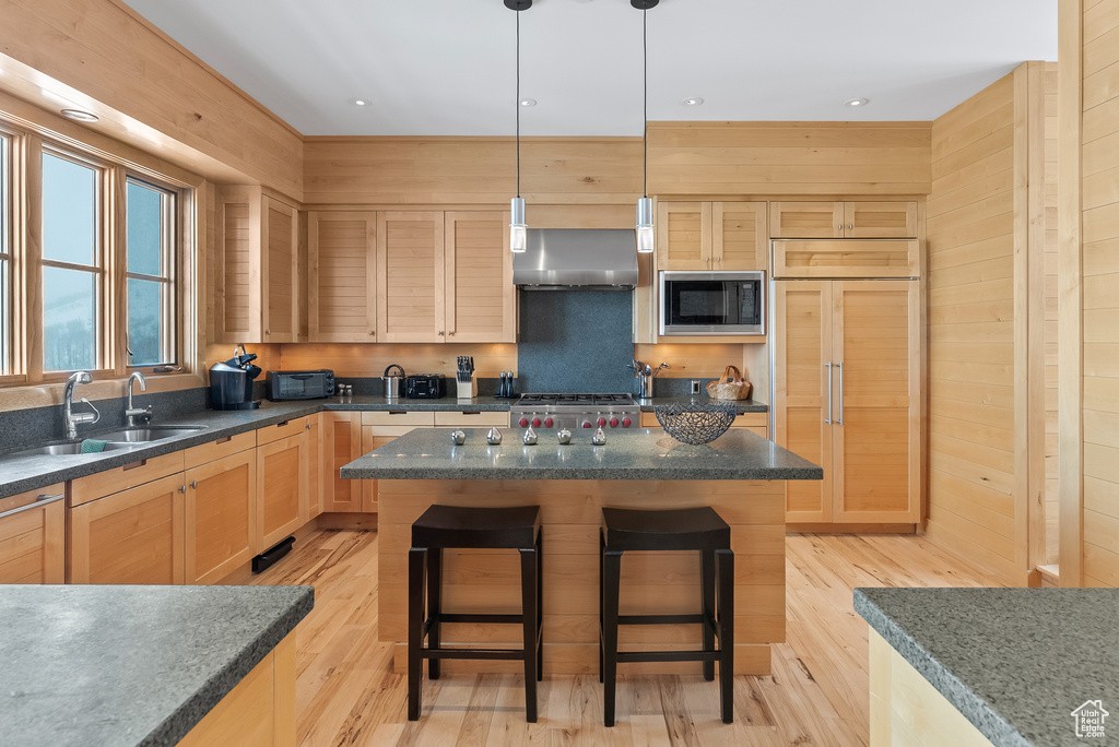 Kitchen featuring hanging light fixtures, wall chimney exhaust hood, a kitchen island, and built in appliances