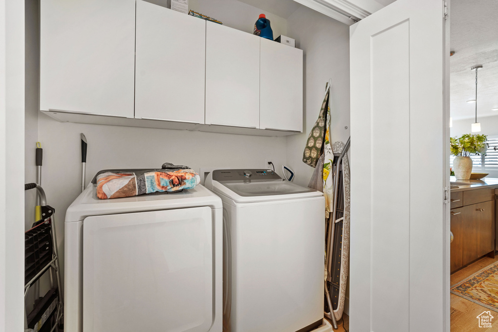 Washroom with hardwood / wood-style flooring, washing machine and dryer, and cabinets