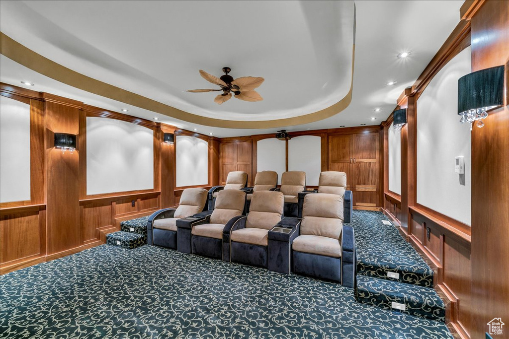Carpeted cinema room with wooden walls, ceiling fan, and a raised ceiling