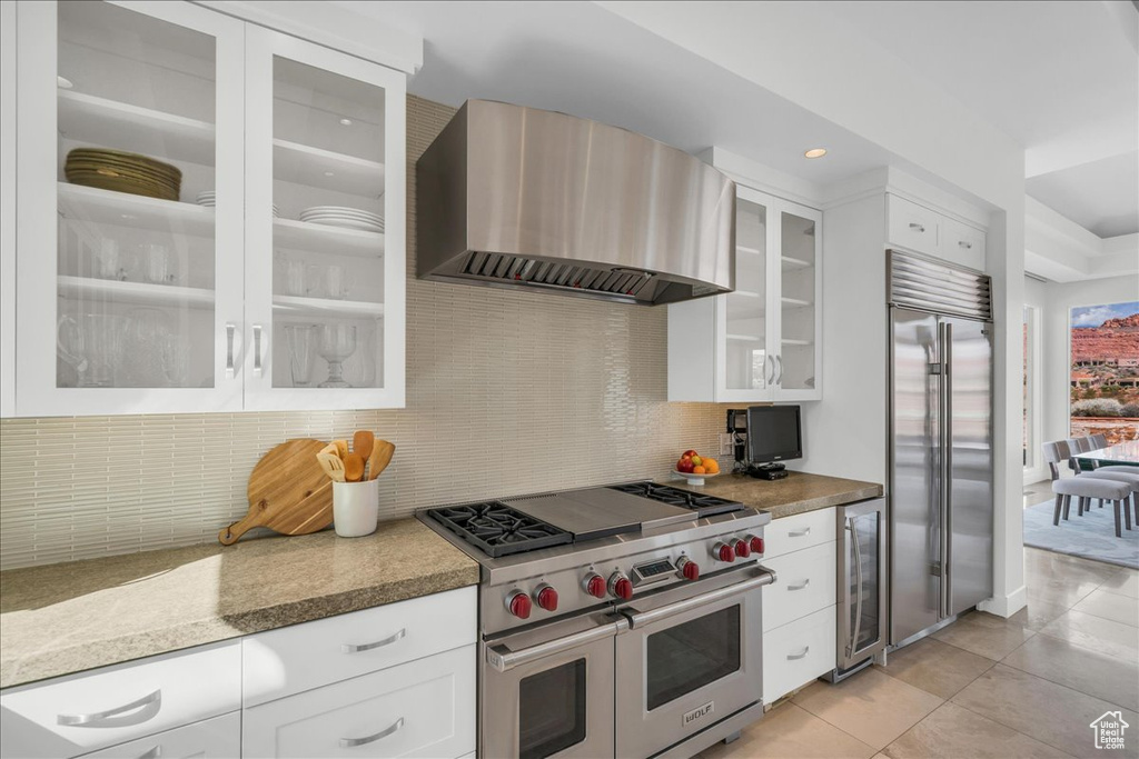 Kitchen with white cabinets, backsplash, high end appliances, wall chimney range hood, and beverage cooler