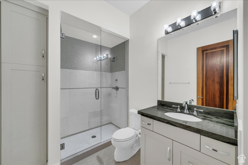 Bathroom with vanity with extensive cabinet space, an inviting chandelier, toilet, a shower with shower door, and tile floors