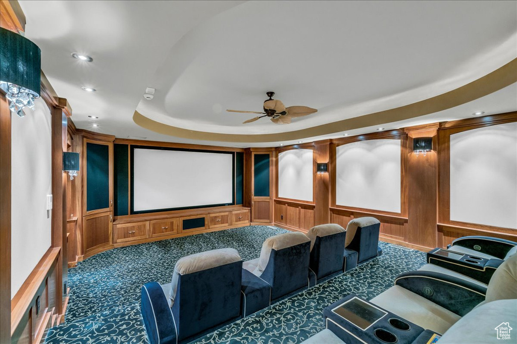 Carpeted home theater room featuring ceiling fan and a raised ceiling