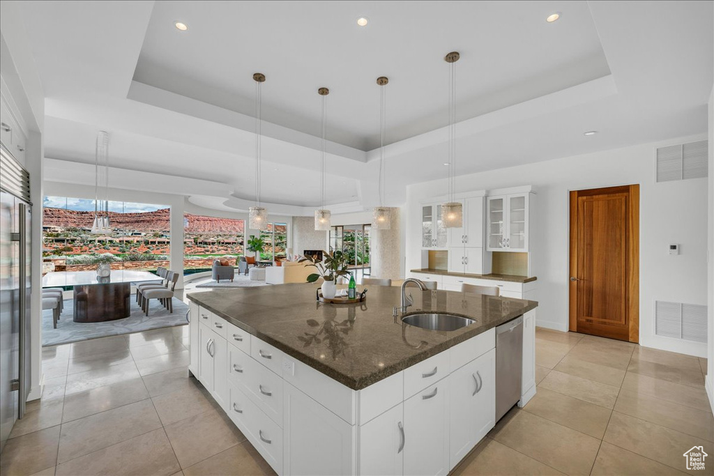 Kitchen featuring sink, a raised ceiling, an island with sink, and decorative light fixtures