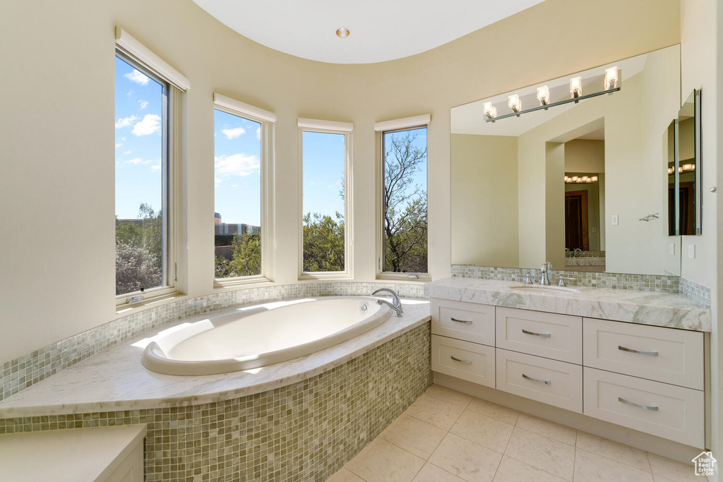Bathroom with tiled bath, vanity with extensive cabinet space, and tile flooring