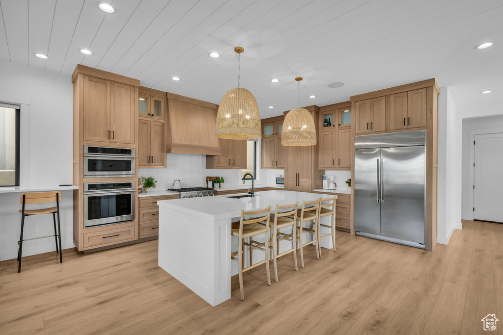 Kitchen featuring light hardwood / wood-style floors, a breakfast bar, stainless steel appliances, and a kitchen island with sink
