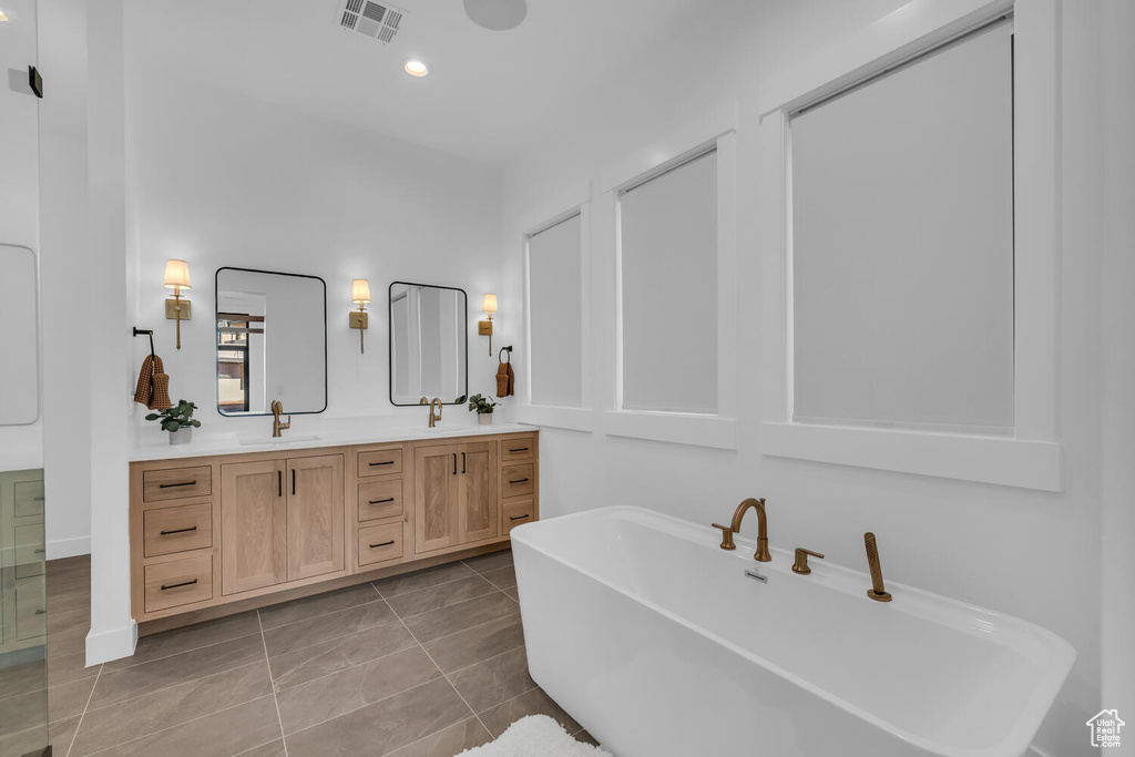 Bathroom featuring dual sinks, tile flooring, a bath to relax in, and vanity with extensive cabinet space