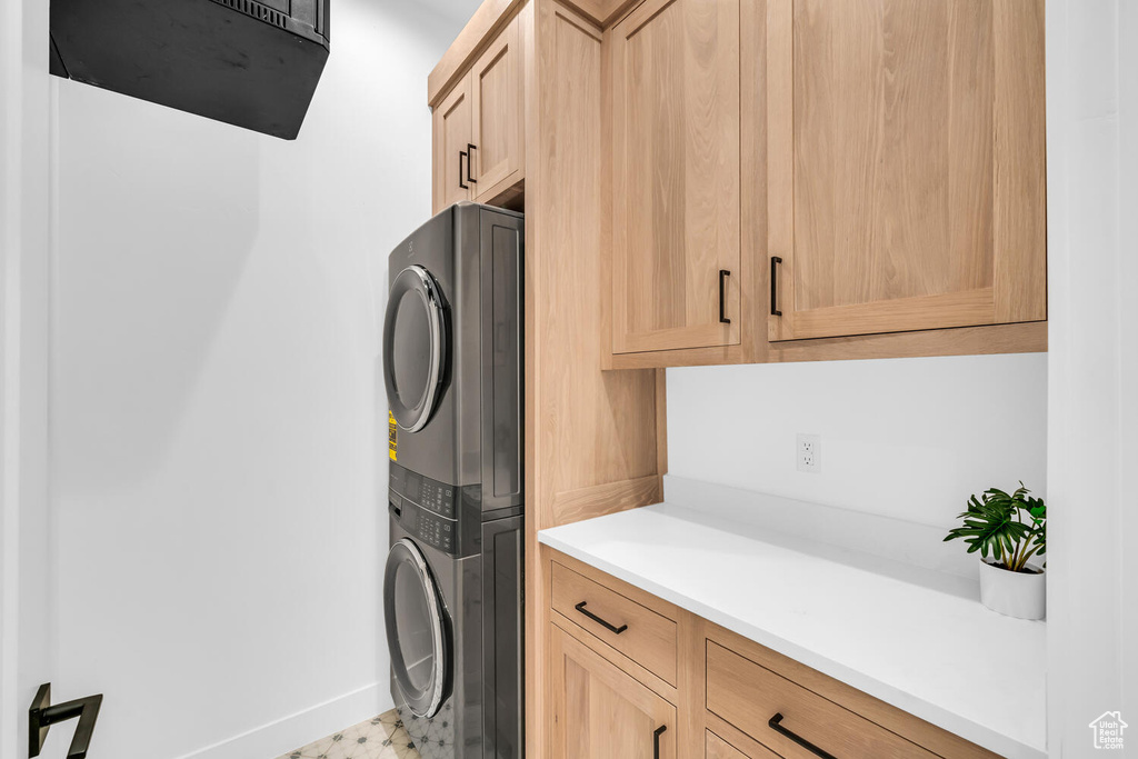Laundry area featuring cabinets, light tile flooring, and stacked washer and dryer