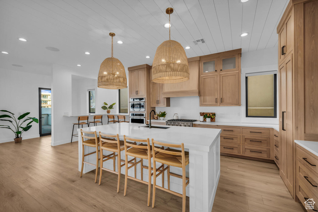 Kitchen featuring a center island with sink, light wood-type flooring, sink, stainless steel appliances, and decorative light fixtures