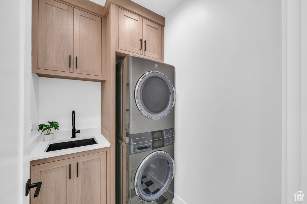 Washroom featuring stacked washer / drying machine, cabinets, and sink