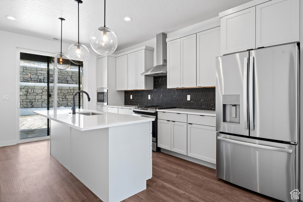 Kitchen featuring dark hardwood / wood-style floors, sink, pendant lighting, appliances with stainless steel finishes, and wall chimney range hood