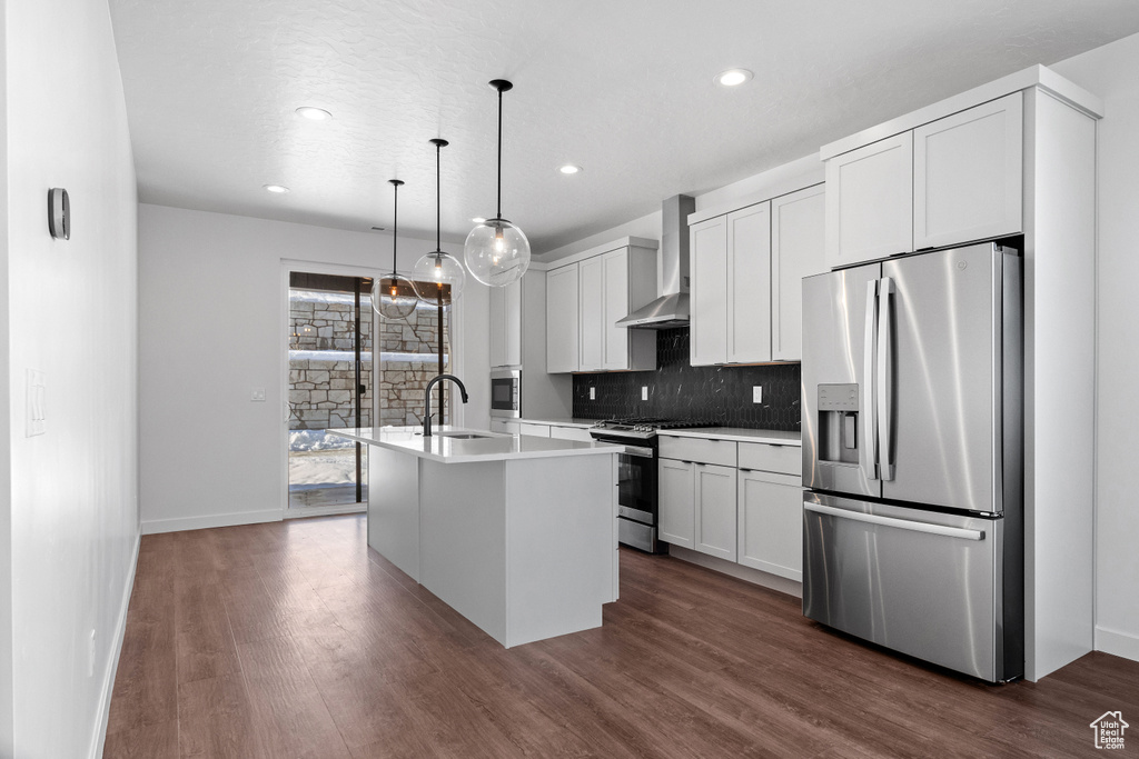 Kitchen featuring wall chimney exhaust hood, pendant lighting, dark hardwood / wood-style flooring, stainless steel appliances, and a kitchen island with sink