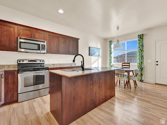 Kitchen featuring light wood-type flooring, hanging light fixtures, stainless steel appliances, and sink