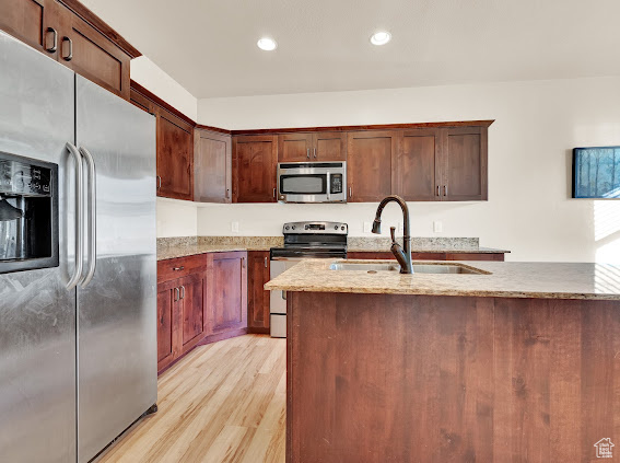 Kitchen with sink, light stone countertops, stainless steel appliances, and light wood-type flooring